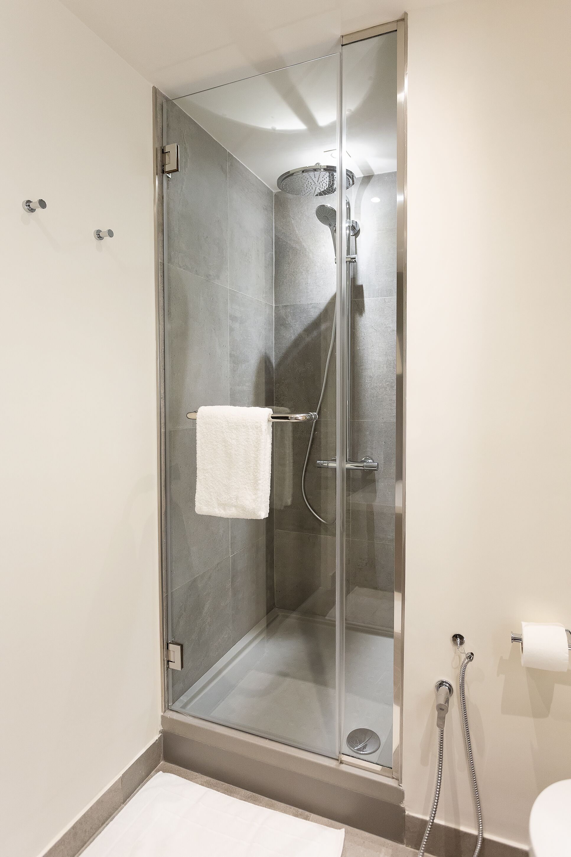 A glass-enclosed shower with a white towel hanging on the door handle, a handheld showerhead, and a wall-mounted faucet.