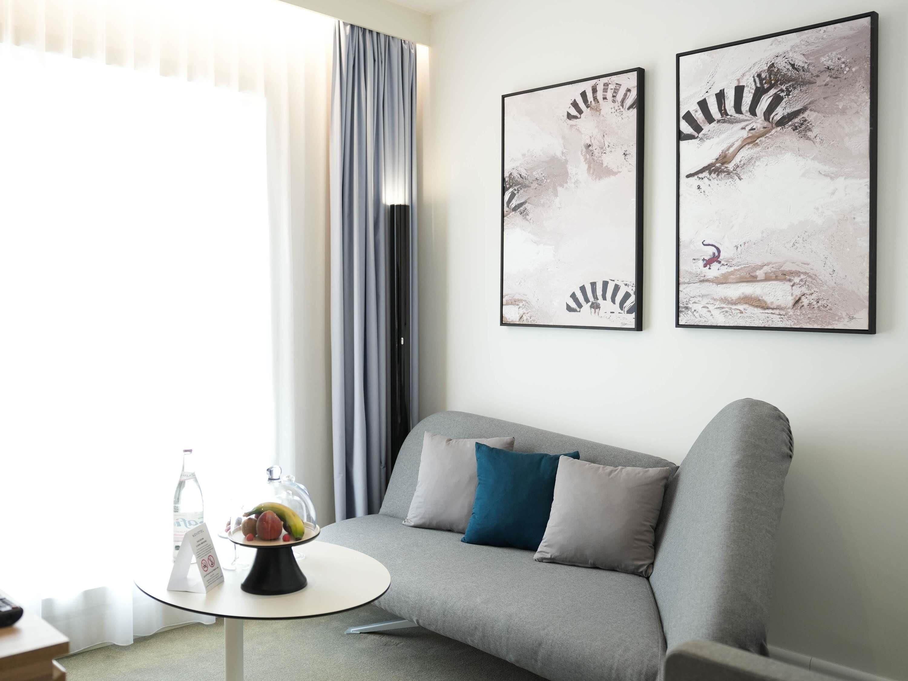 Una sala de estar moderna con un sofá gris, una mesita redonda con un frutero y dos cuadros abstractos en la pared.
