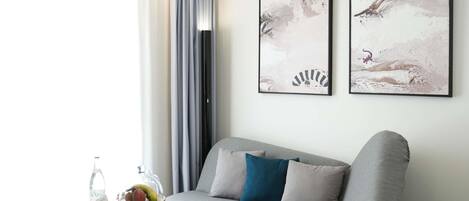 A modern living room with a grey sofa, a small round table with a fruit bowl, and two abstract paintings on the wall.