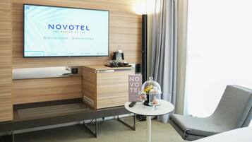 A hotel room with a television displaying 'NOVOTEL' and a sign indicating 'ROOM SERVICE.'