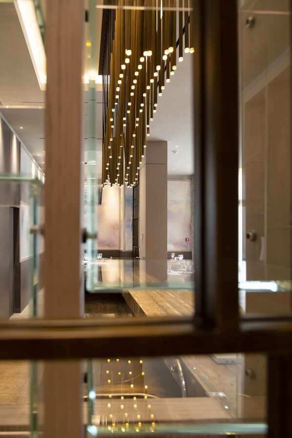 A modern interior with a glass railing, a hanging light fixture, and a view of a bathroom. - Novotel Tunis Lac (Tunis)