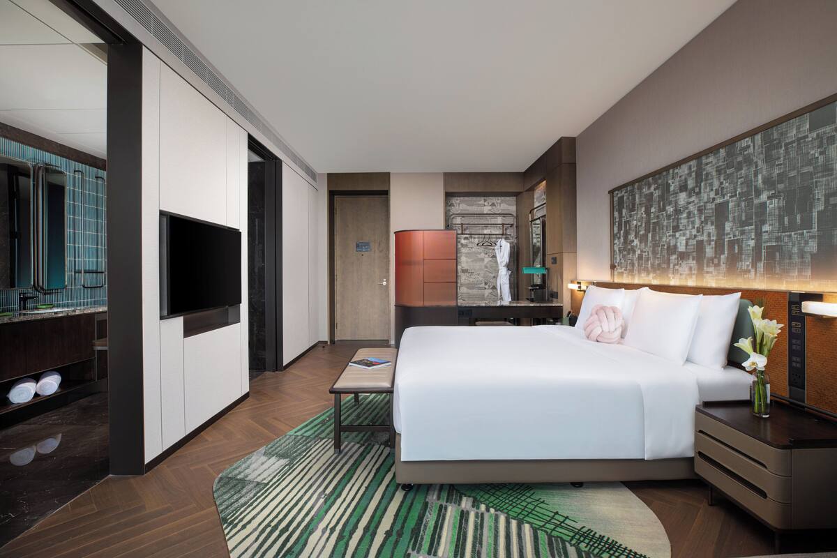 A modern hotel room with a large bed, a flat-screen TV, a desk, and a bathroom with a shower and toilet.