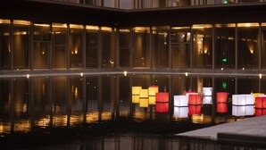 Superficie acuática reflectante con faroles iluminados y fachada de un edificio moderno.