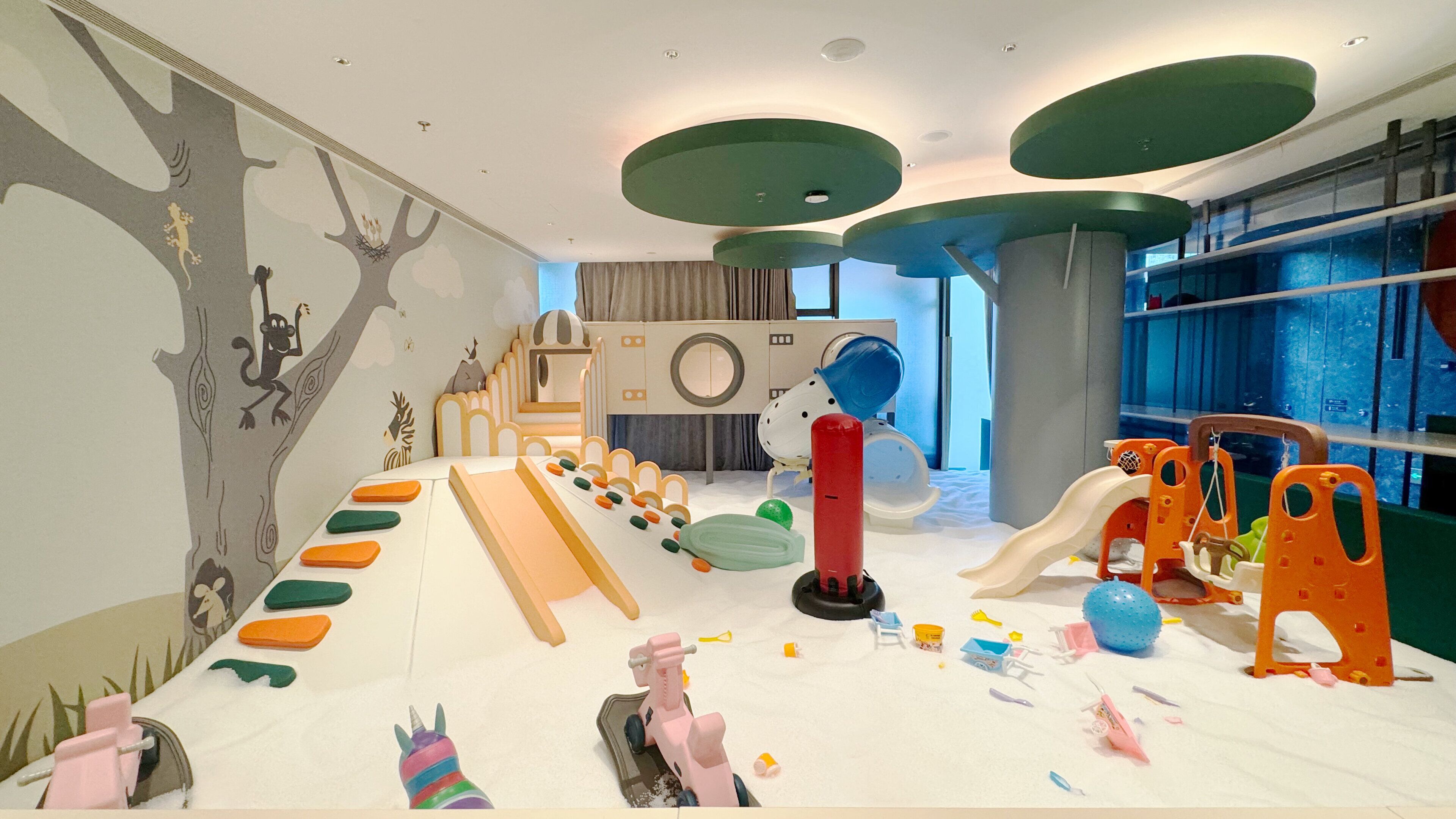 A children's play area with a slide, climbing structures, and a colorful wall mural.