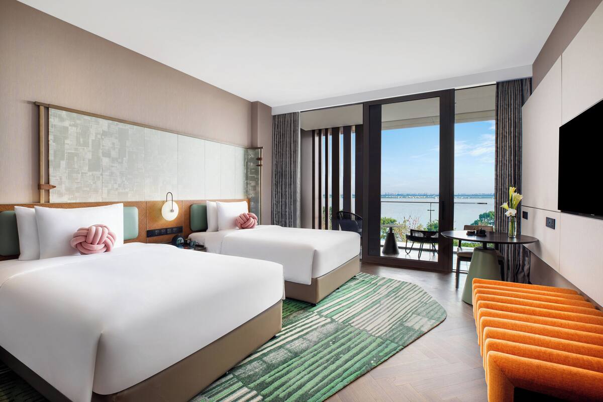 A hotel room with two beds, a balcony with a view, a dining area, and a TV.