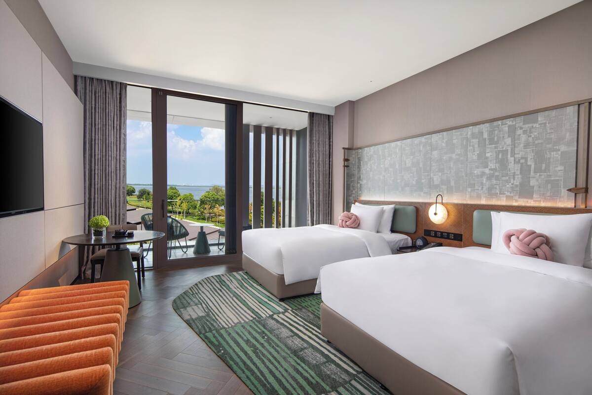 A hotel room with two beds, a TV, a balcony with a view, and a dining area.