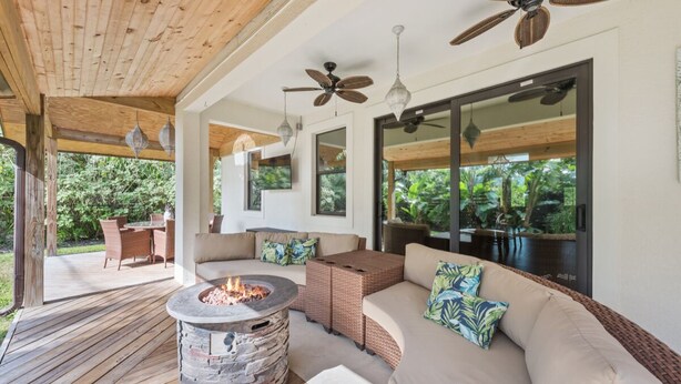 An outdoor living area with a stone fire pit, wicker furniture, ceiling fans, and large windows offering a view of the outdoors. - * Welcome to Relaxa * (Naples)