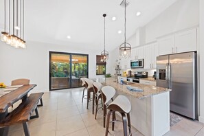 A modern kitchen with white cabinets, stainless steel appliances, and a central island with bar stools. - * Welcome to Relaxa * (Naples)