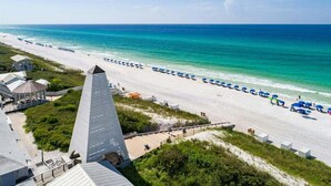 A beach with a long row of blue umbrellas and a tall, narrow building in the foreground. - 1 HOUSE OFF BEACH w/ LSV, BIKES, POOL & GULF VIEWS! PET FRIENDLY! (Santa Rosa Beach)