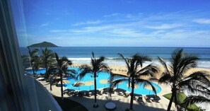 Blick auf einen Strandort mit Pool, Palmen und einer entfernten Insel.