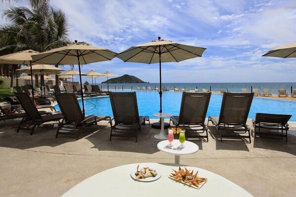 A poolside area with lounge chairs and umbrellas, a table with drinks, and a view of the sea.