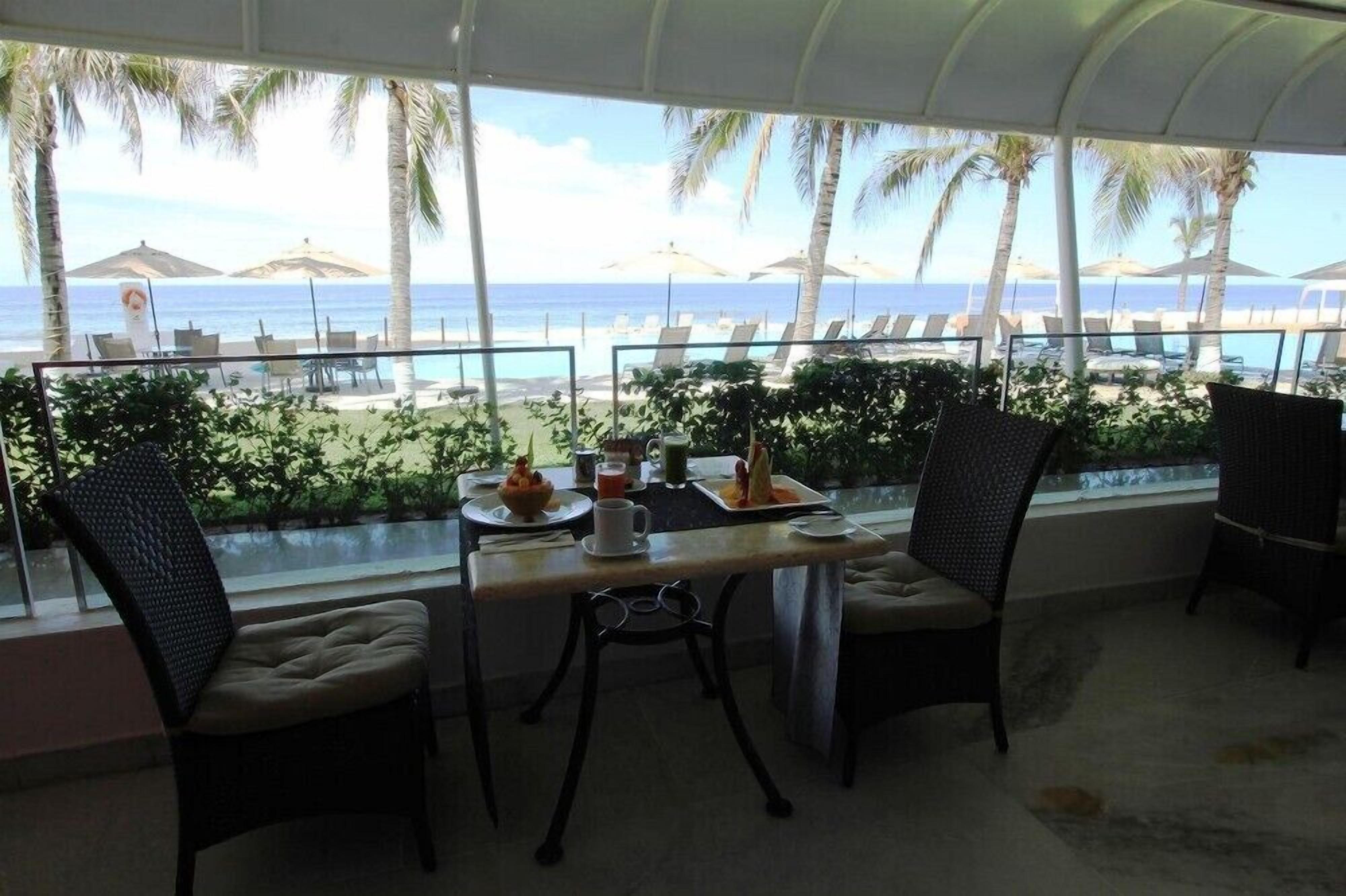 A dining area with a view of the beach, featuring a table with chairs and a view of the ocean.