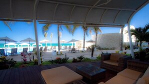A covered outdoor seating area with lounge chairs and umbrellas, overlooking a pool and beach. - Tasteful Junior Suite with a Terrace and Private Beach Area (Marina Mazatlán)