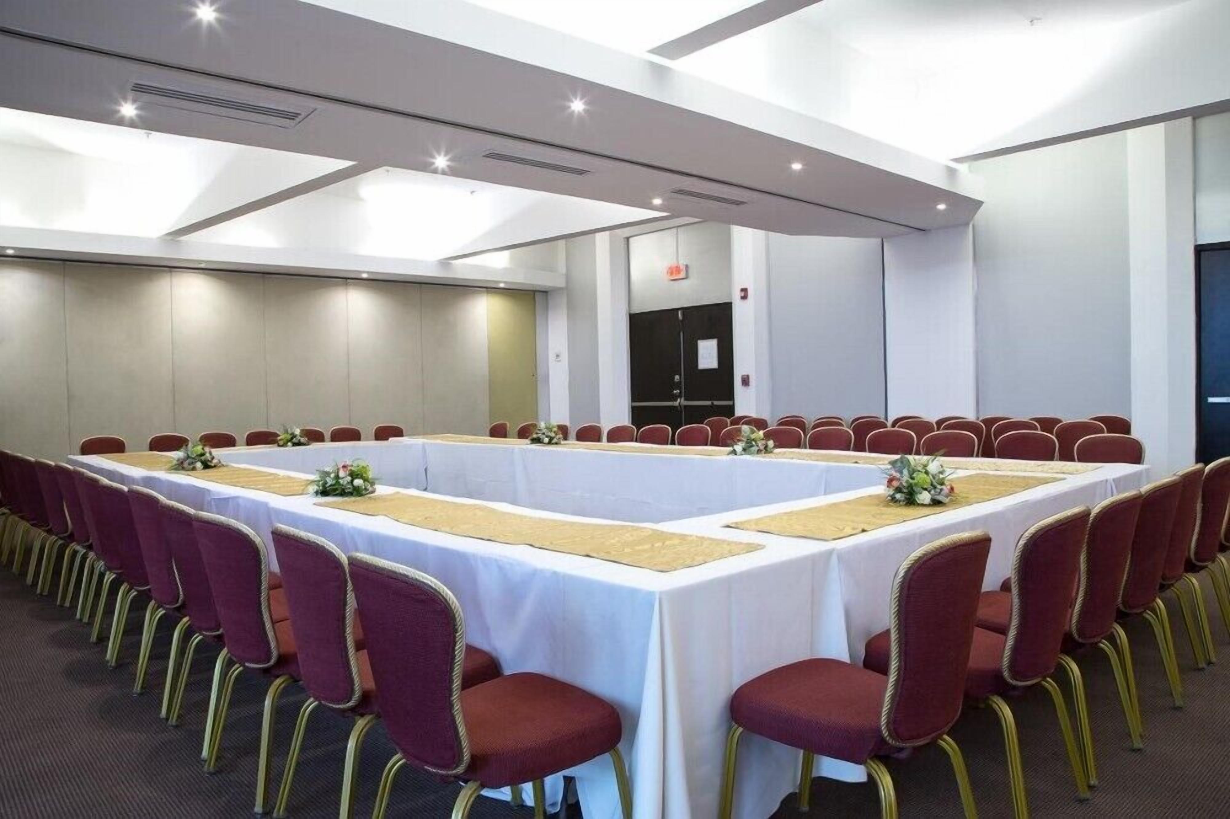 Une salle de conférence avec une longue table, des chaises rouges et des nappes blanches.