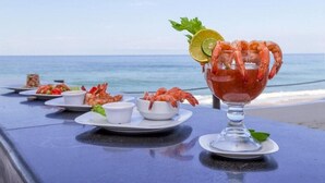 A table set with seafood dishes and a drink garnished with shrimp, lime, and parsley, overlooking the ocean. - Private Junior Suite with a Short Ride Away from Beach (Marina Mazatlán)