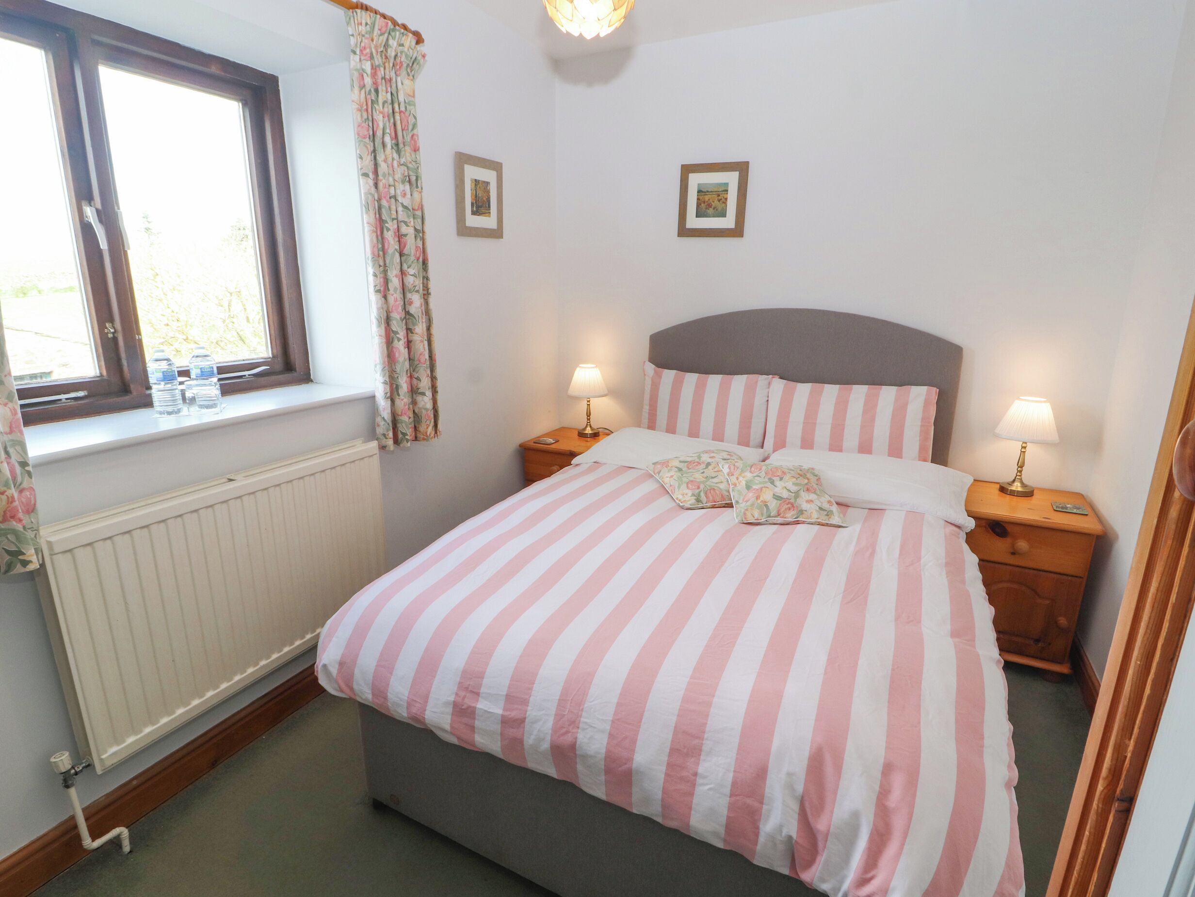 A bedroom with a bed, two bedside tables, a window with curtains, and a radiator.