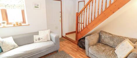 A cozy living room with two sofas, a wooden staircase, and a door leading to another room.