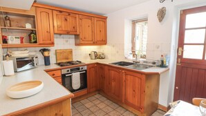 A kitchen with wooden cabinets, a stove, a sink, and a window with blinds. - Barn Cottage (Carnforth)