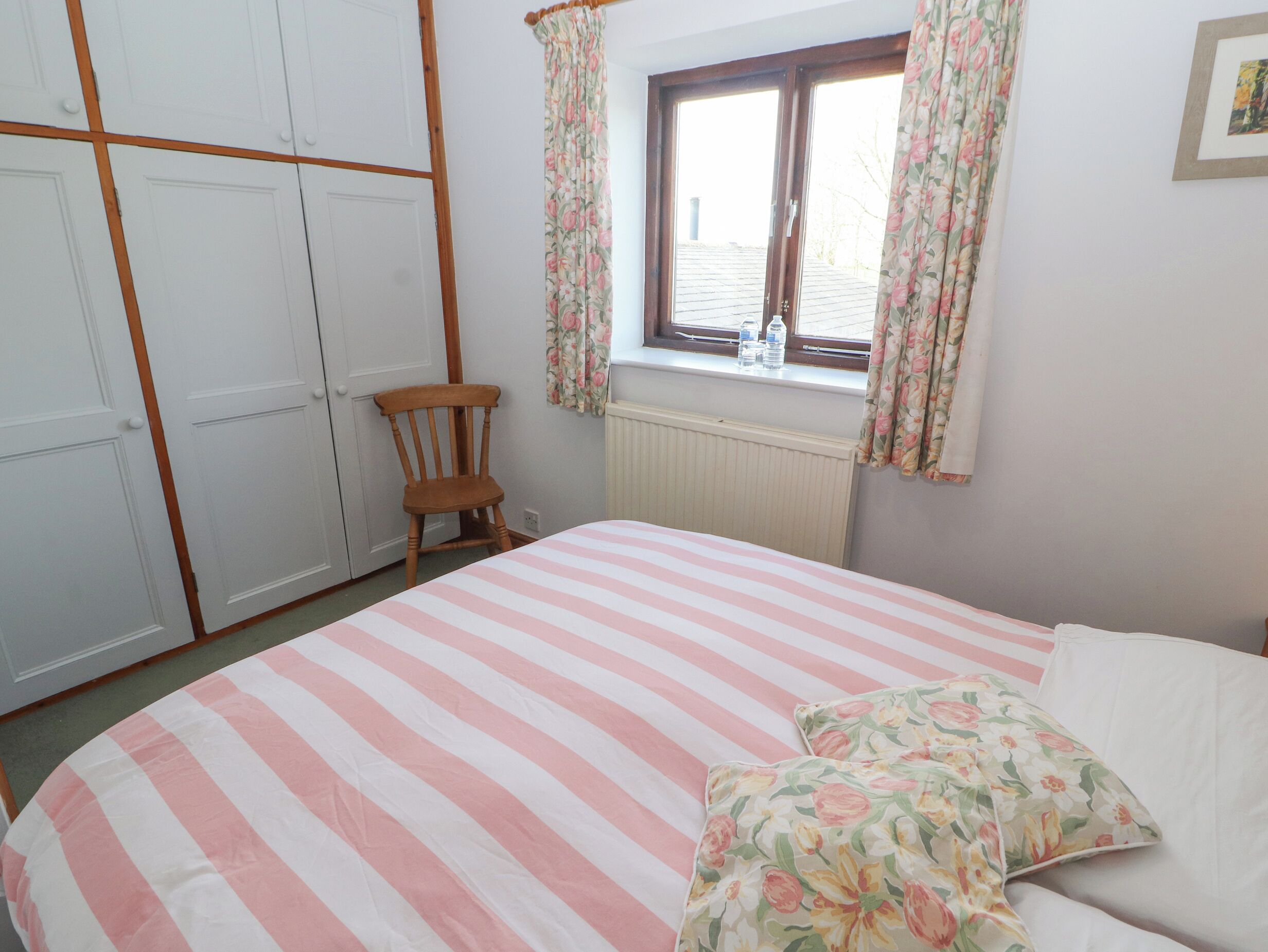 A bedroom with a bed, a chair, a window with curtains, and a radiator.