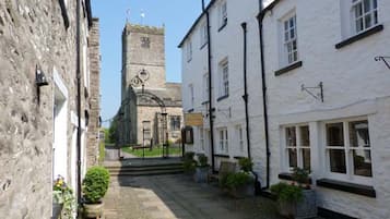 A narrow cobblestone street lined with white buildings, a church with a tall tower, and a gate leading to a courtyard with potted plants.