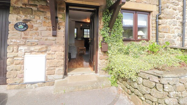 A stone building with a wooden door and a sign reading "Barn Cottage." - Barn Cottage (Carnforth)