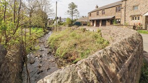 A stone building with a stone wall and a stream. - Barn Cottage (Carnforth)
