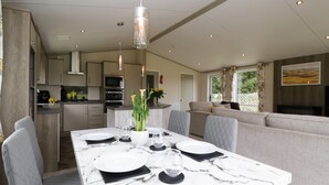 A modern kitchen with a dining area, featuring a marble table, grey upholstered chairs, and pendant lighting. - Hill View, Lilac Lodge (Wareham)