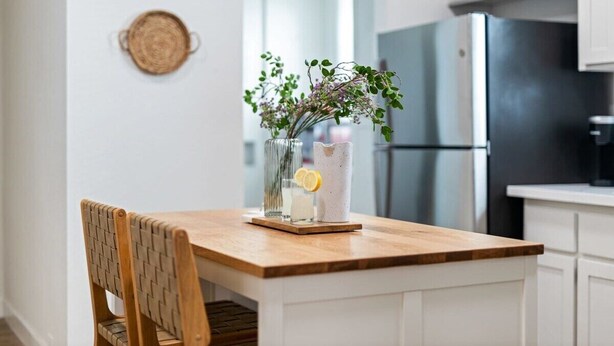 Eine Küche mit einem Holztisch, einem Stuhl, einer Blumenvase und einem Kühlschrank.