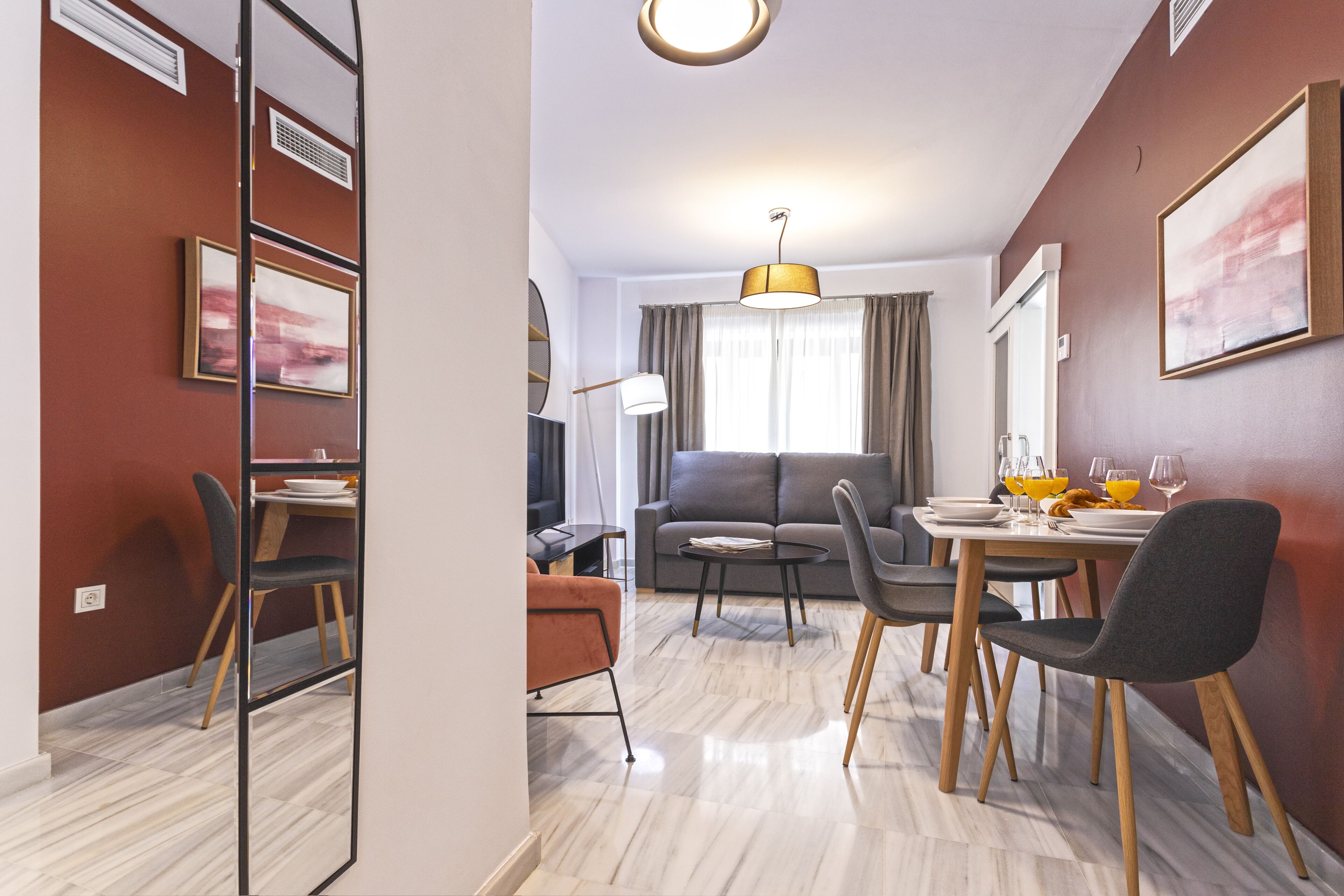 Un espace de repas moderne avec une table dressée pour deux personnes, un canapé et un miroir qui reflète la pièce.