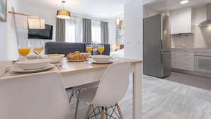 Une cuisine moderne avec des meubles blancs, un réfrigérateur en acier inoxydable et un coin repas comprenant une table en bois et des chaises blanches.