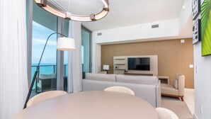 Ein modernes Hotelzimmer mit einem runden Esstisch, einer Couch, einem Fernseher und einem Balkon mit Blick.