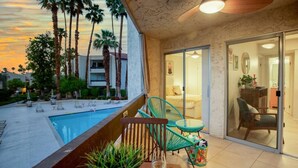 A balcony with a pool, chairs, and a table with a plant and a glass. - Colorful, Modern Condo at the famed Biltmore (Palm Springs)