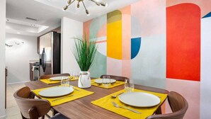 A dining area with a wooden table set for four, yellow placemats, and a potted plant. - Colorful, Modern Condo at the famed Biltmore (Palm Springs)