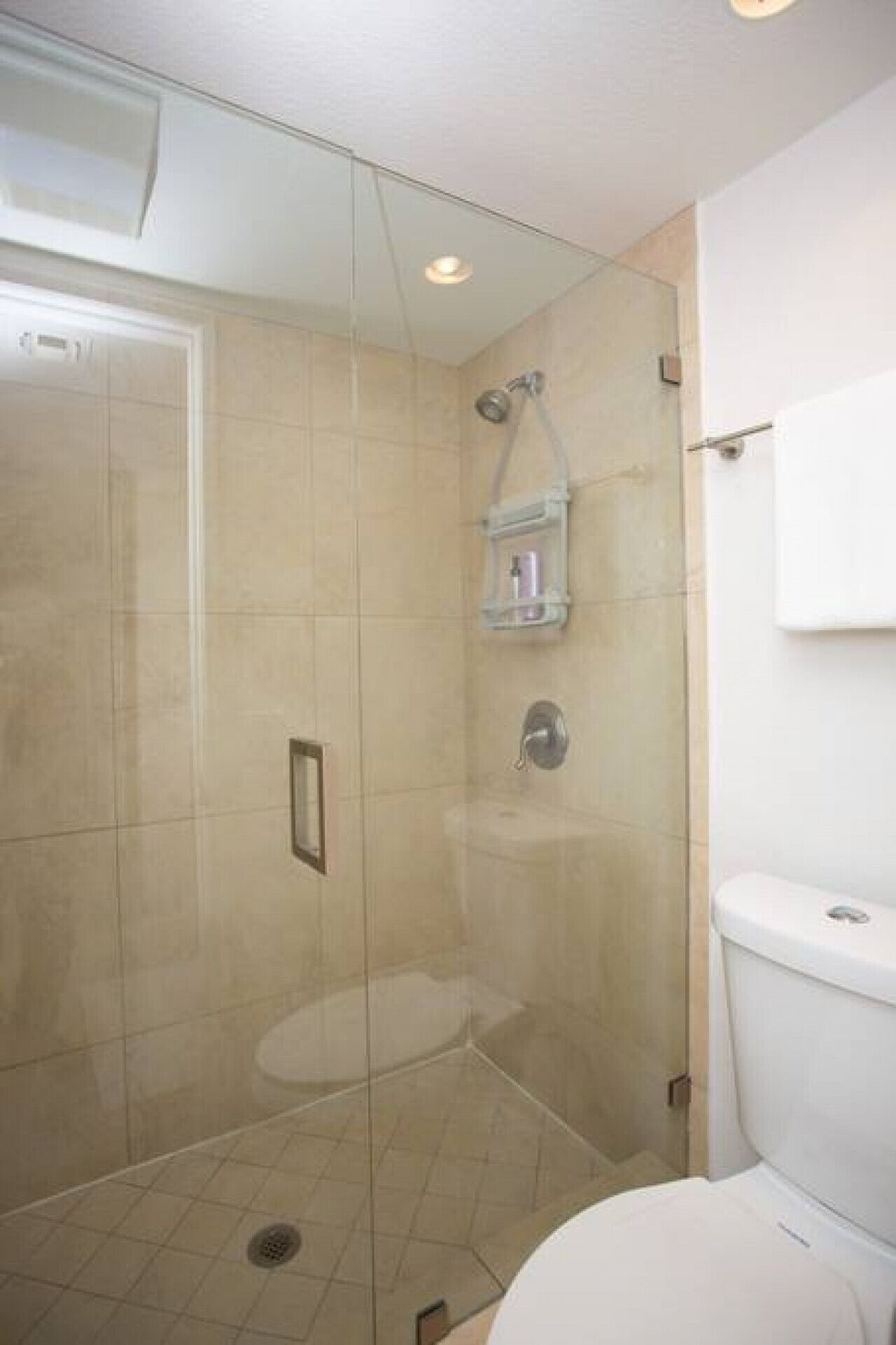 A modern bathroom with a glass-enclosed shower, a toilet, and a small shelf with toiletries.
