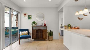 A modern kitchen with a wooden cabinet, a blue chair, and a dining area with a glass door leading outside. - Colorful, Modern Condo at the famed Biltmore (Palm Springs)
