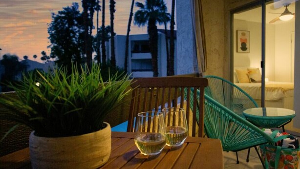A wooden table with two glasses of white wine, a potted plant, and a green chair. - Colorful, Modern Condo at the famed Biltmore (Palm Springs)