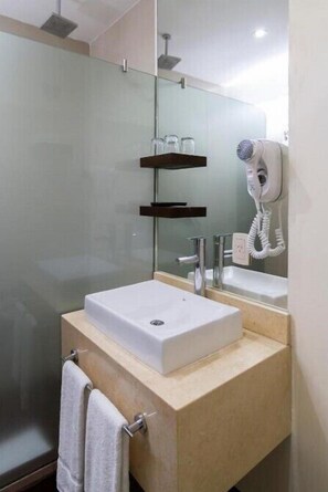 Een moderne badkamer met een glazen douchecabine, een witte wastafel, een haardroger en een handdoekrek.