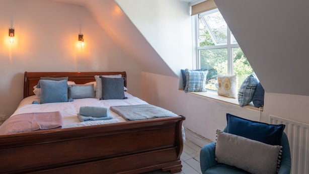 Une chambre avec un lit en bois, des oreillers, une chaise et une fenêtre donnant sur un paysage agréable.