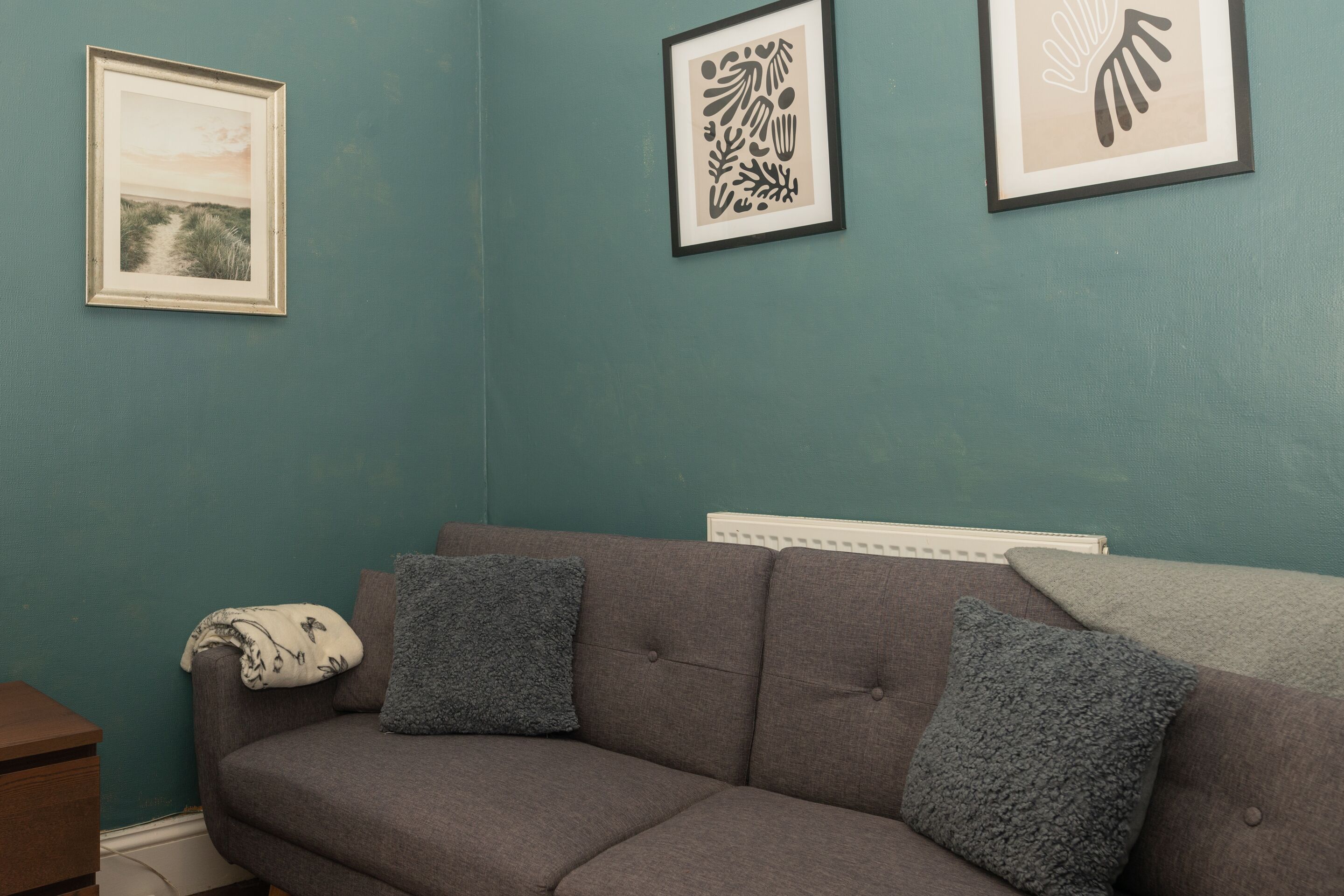 Una habitación con paredes verde azulado, un sofá gris con dos cojines grises, y tres obras de arte enmarcadas en la pared.