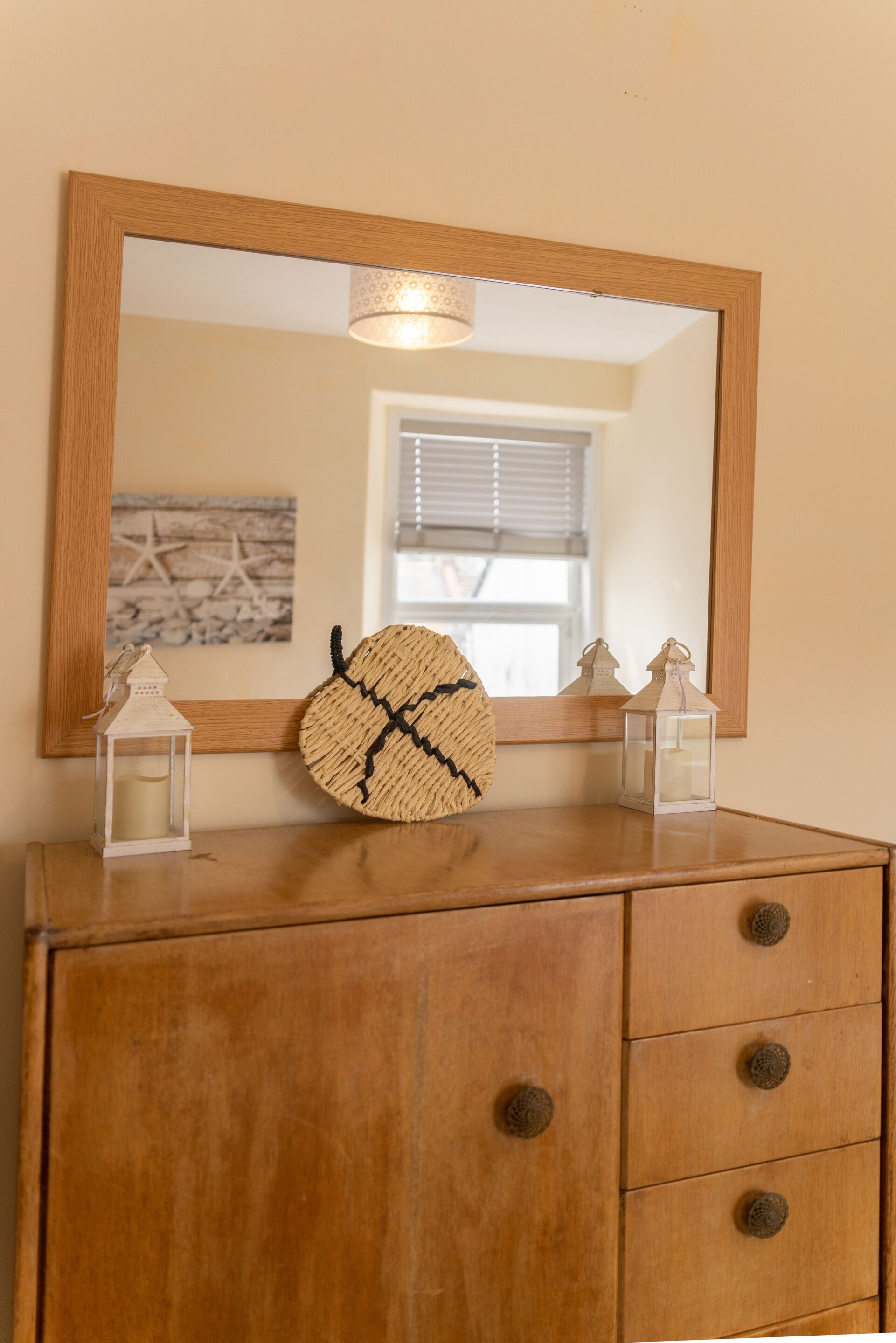 A wooden dresser with a mirror above it, two small lanterns, and a woven basket.