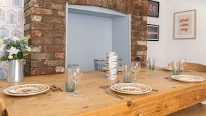 Une table de salle à manger en bois, mise avec des assiettes, des couverts et des verres, avec un mur de briques et un panneau encadré en arrière-plan.