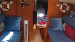 A compact cabin with two blue upholstered sofas, a wooden table, and a small bed with a floral bedspread.