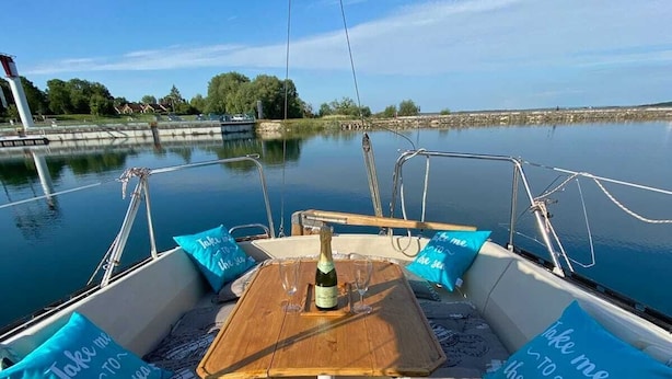 A boat's deck with a wooden table, two blue cushions with text, and a bottle of wine.