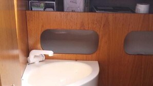 A compact bathroom with a white sink, toilet, and a small shelf above the sink.
