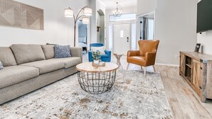 A modern living room with a sofa, armchair, coffee table, and a TV on a wooden cabinet. - Remodeled home in quiet neighborhood--kid friendly (Edmond)