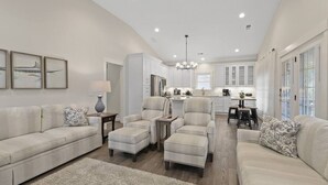 A spacious living room with a sofa, armchairs, and a coffee table. There is a kitchen in the background with cabinets and a dining area. - Luxury in a Prime Folly Location! Walk everywhere! (Folly Beach)