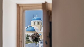 A view through a doorway of a building with blue domed structures, possibly a church or temple, and a small tree with pink flowers. - The Mill Haven Santorini (Santorini)