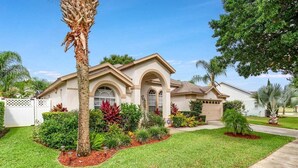 A single-story house with a front yard, palm trees, and a variety of shrubs.