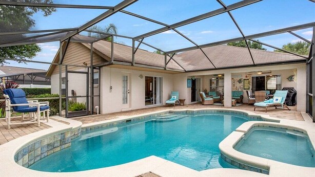 A swimming pool with a covered patio area, lounge chairs, and a clear sky.