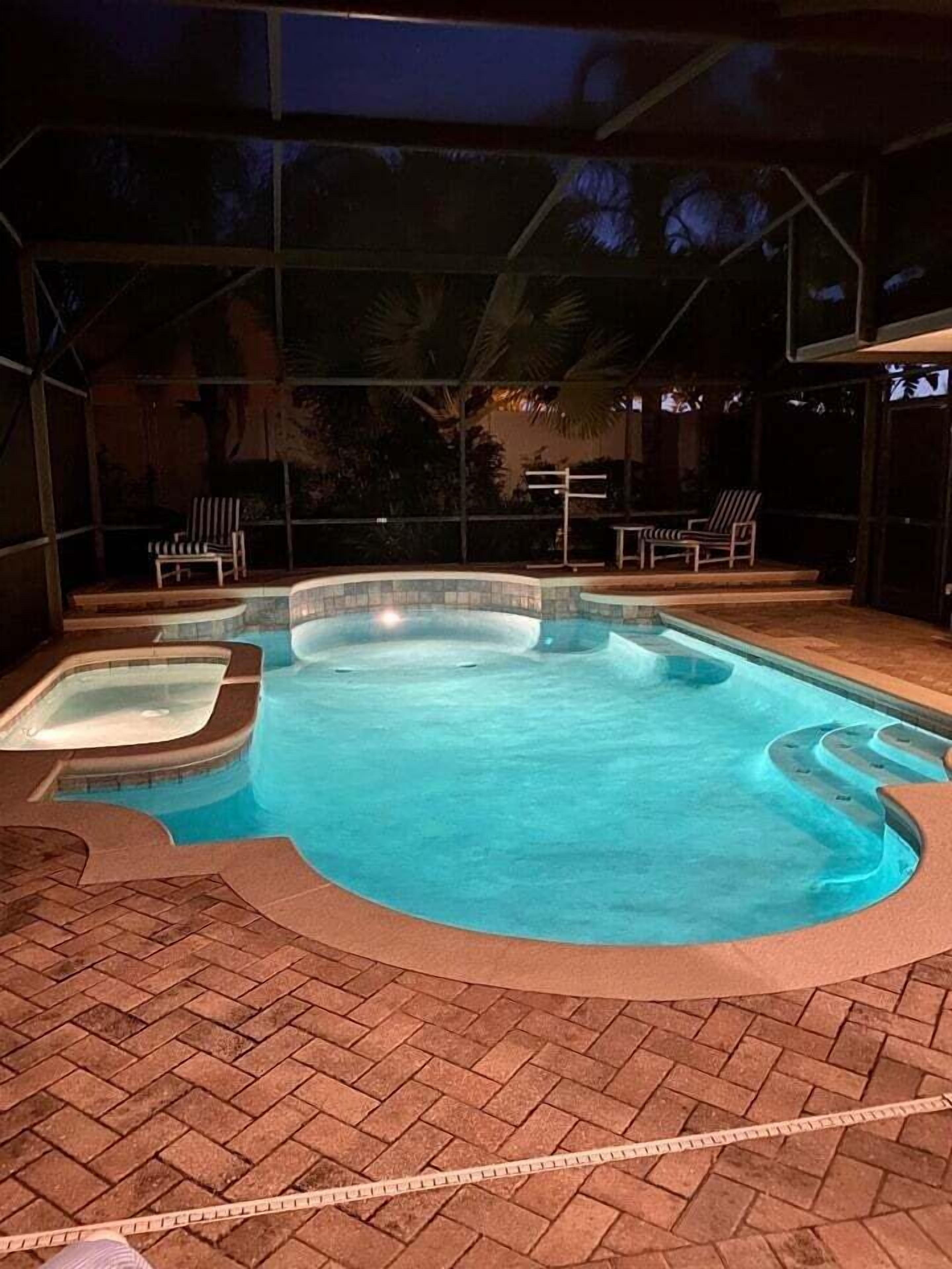 Piscina con un jacuzzi, rodeada por un patio de ladrillo y una zona cubierta con sillas.